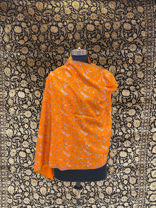 Orange patterned shawl on a mannequin against a black floral background