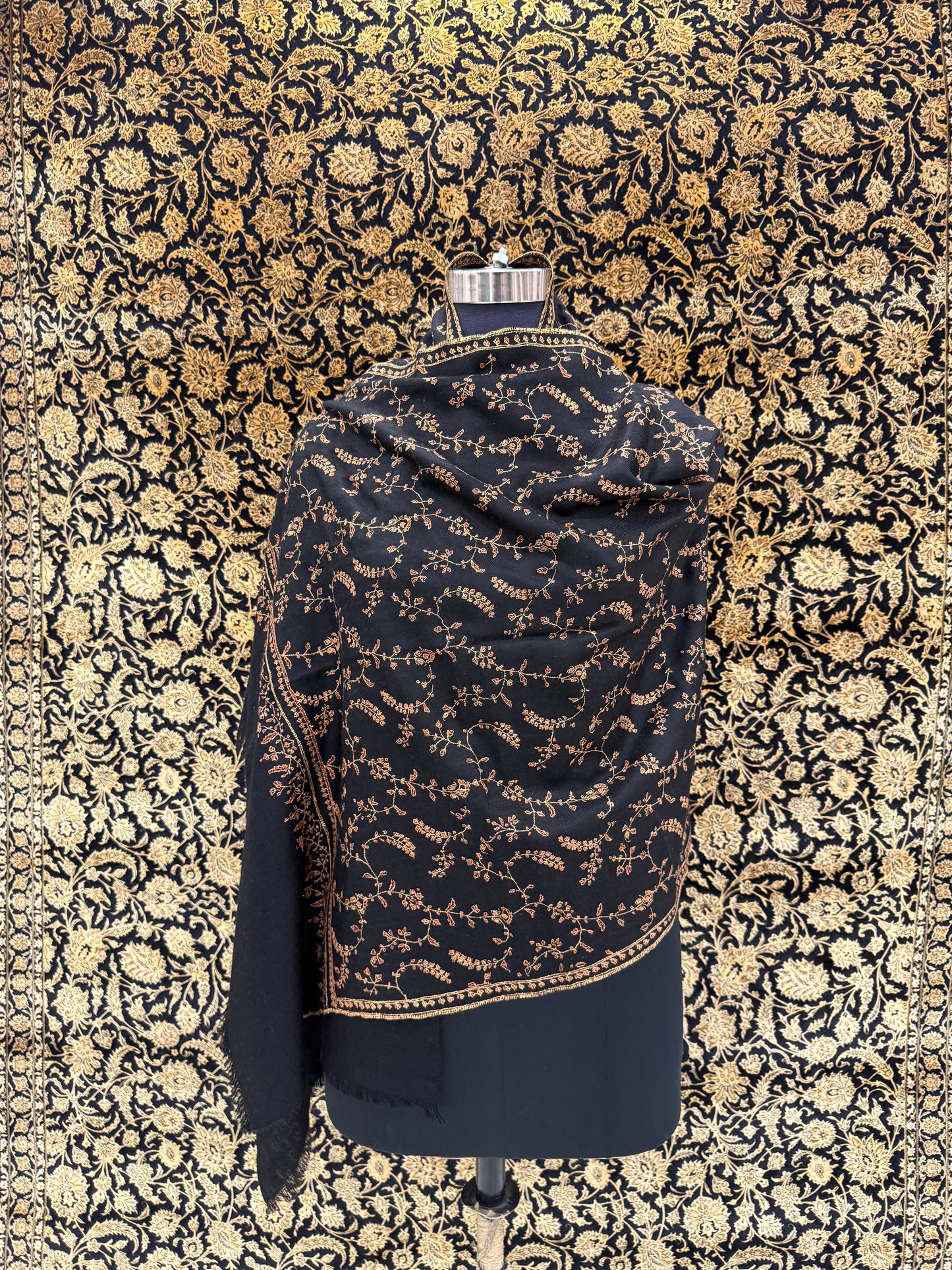 Black and gold patterned fabric on a mannequin against a floral patterned wall.