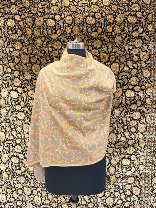 Mannequin wearing a beige shawl with orange floral patterns against a black and gold patterned background