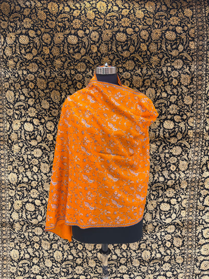 Orange patterned shawl on a mannequin against a black floral background