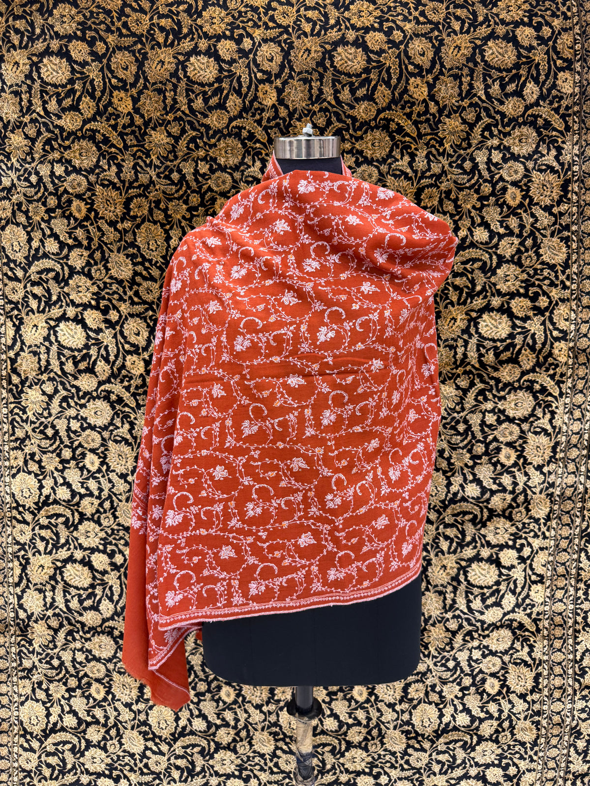 Red patterned fabric draped over a mannequin against a decorative black and gold background