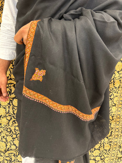 Black garment with orange embroidery on a patterned fabric background
